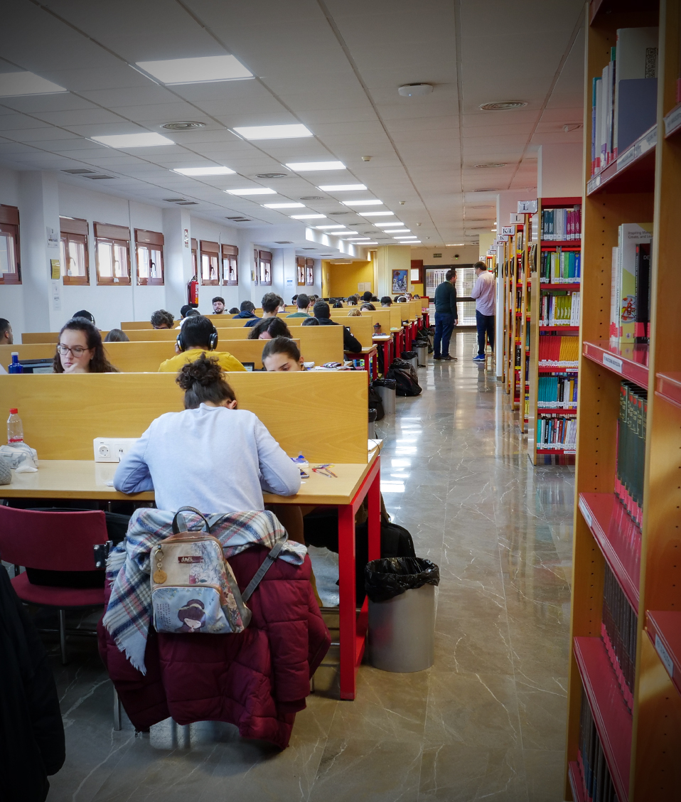 Biblioteca de la Facultad de Informática y Telecomunicaciones con estanterías de libros a la derecha y estudiantes a la izquierda